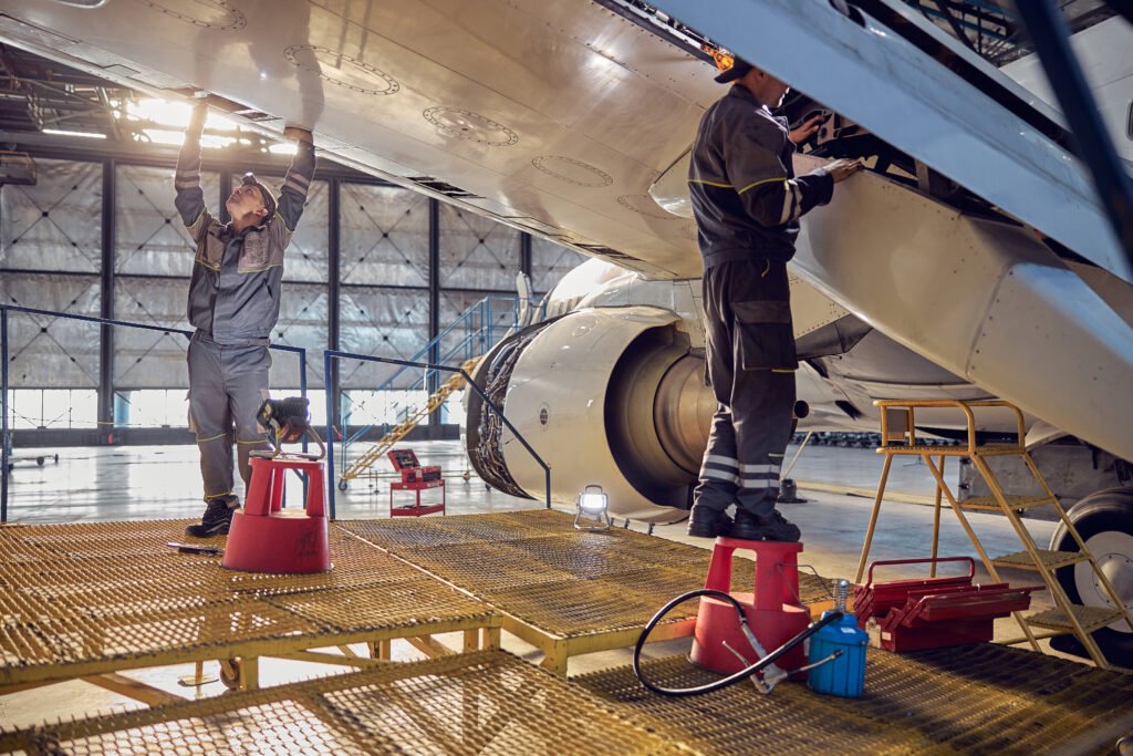 Full length side view portrait of men aviation mechanics fixing and checking spoiler and flaps on the airplane. Aviation Recruitment demand.