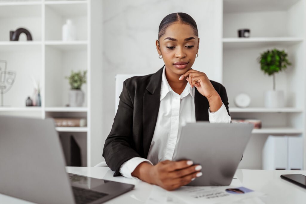 Confident black woman in formal wear using digital tablet, chatting on gadget for business in office interior. Planning startup, businesswoman work, app and gadget, lifestyle. Hiring Aviation Professionals