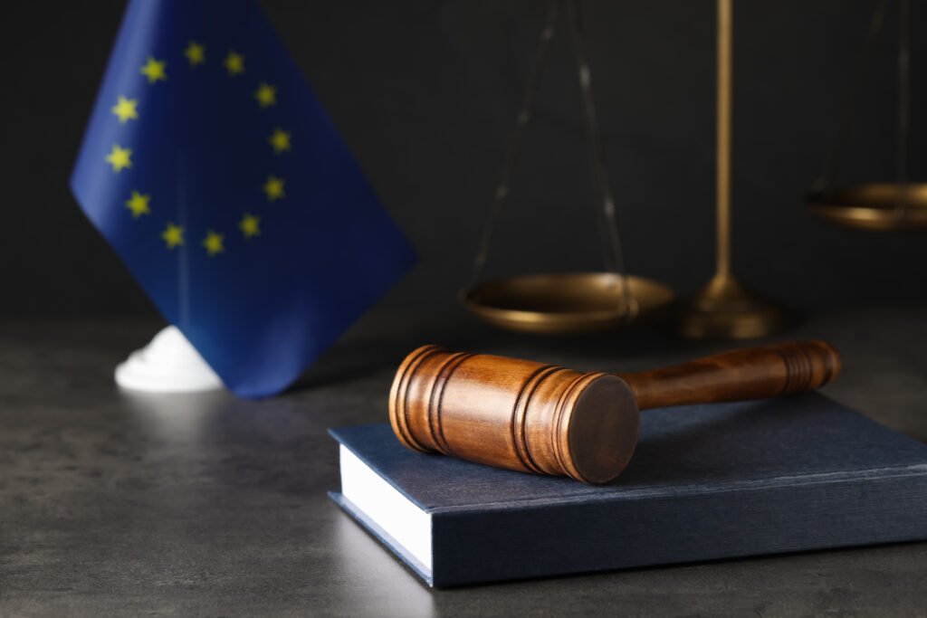 Wooden judge's gavel and book on grey table near European Union flag. Space for text. Board-Level Internal Investigations