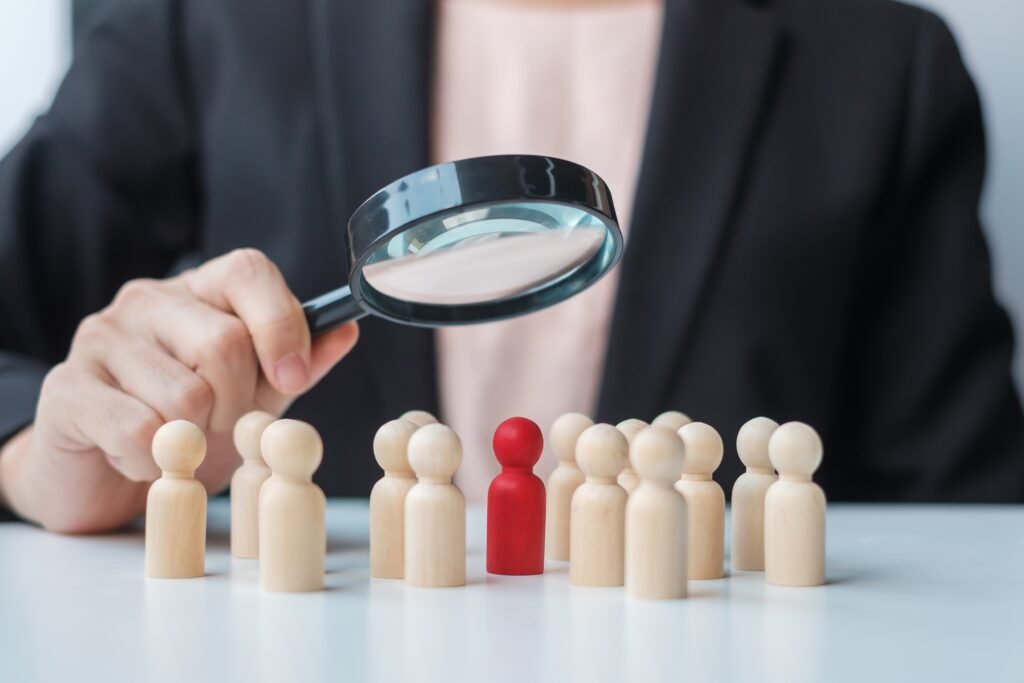 Businesswoman hand holding magnifying glass for recruiting leader man wooden from crowd of employees.Human resource management, Recruitment, Teamwork, hiring and leadership Concepts. Board-Level Internal Investigations